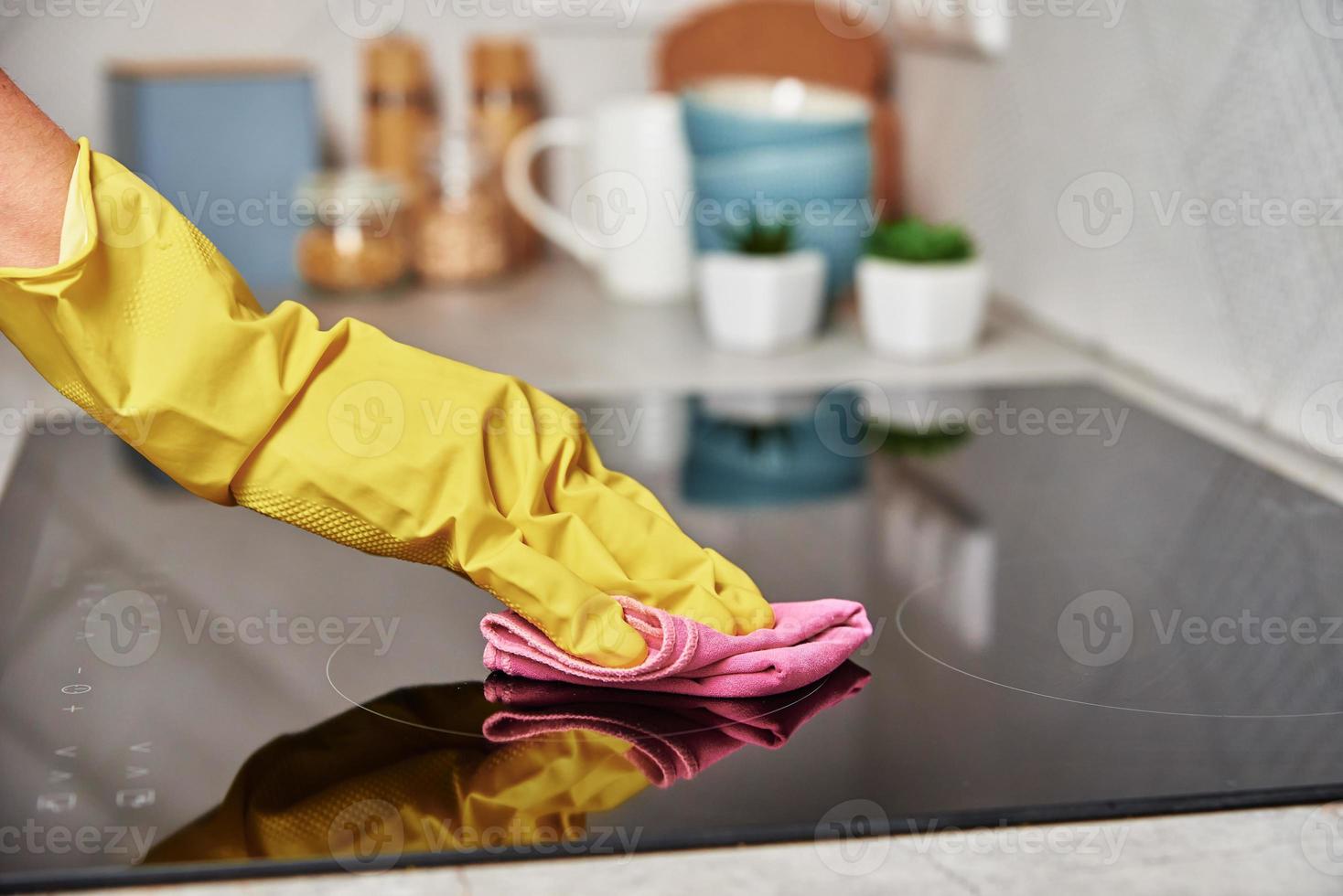 mujer con guantes de goma limpiando estufa de inducción foto