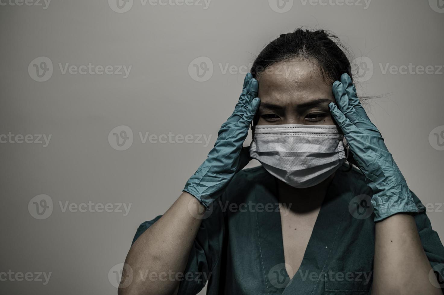 una enfermera asiática cansada y deprimida usa una máscara facial uniforme azul sentada en el piso del hospital, una joven doctora estresada por el trabajo duro foto