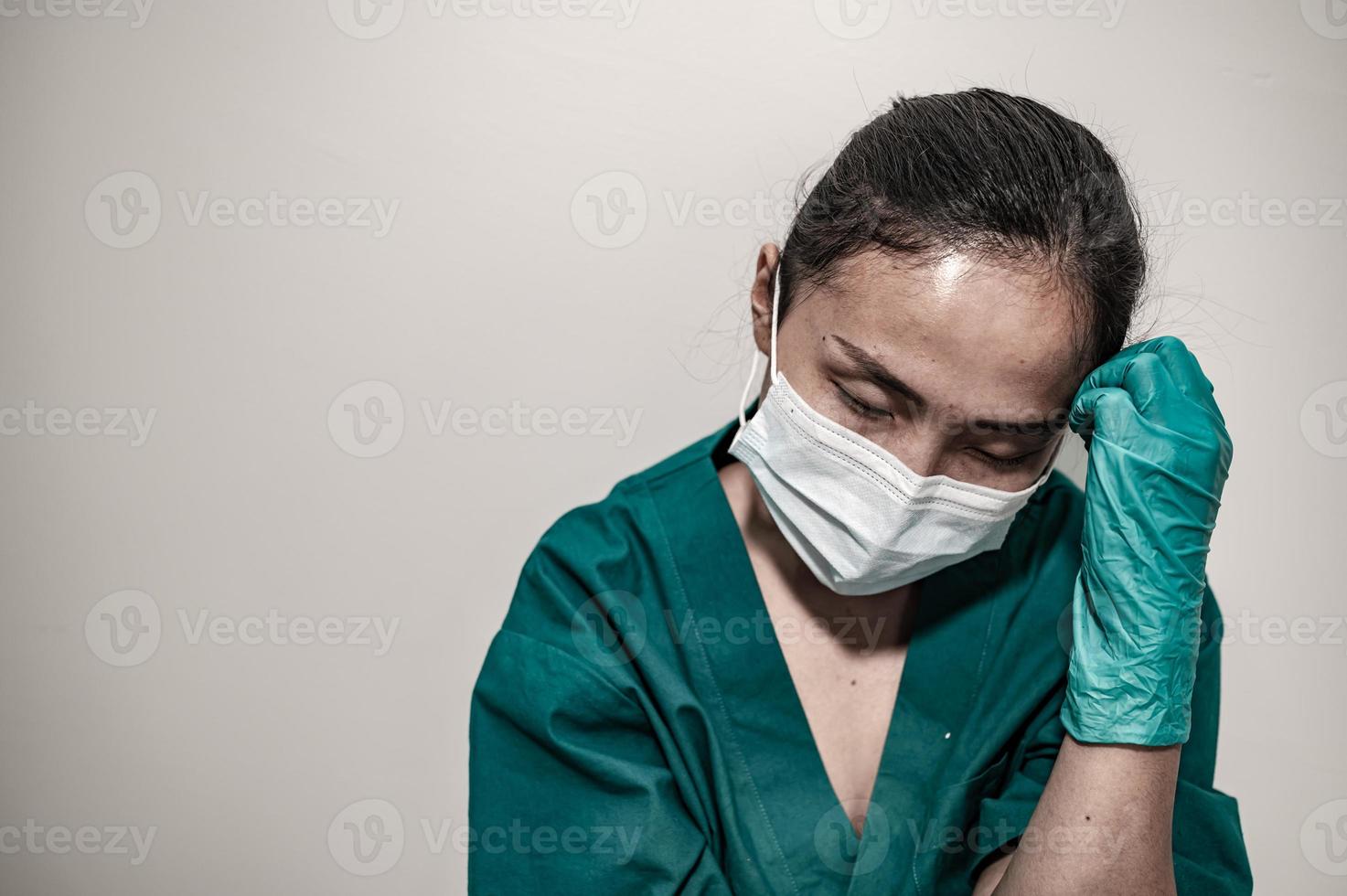 una enfermera asiática cansada y deprimida usa una máscara facial uniforme azul sentada en el piso del hospital, una joven doctora estresada por el trabajo duro foto