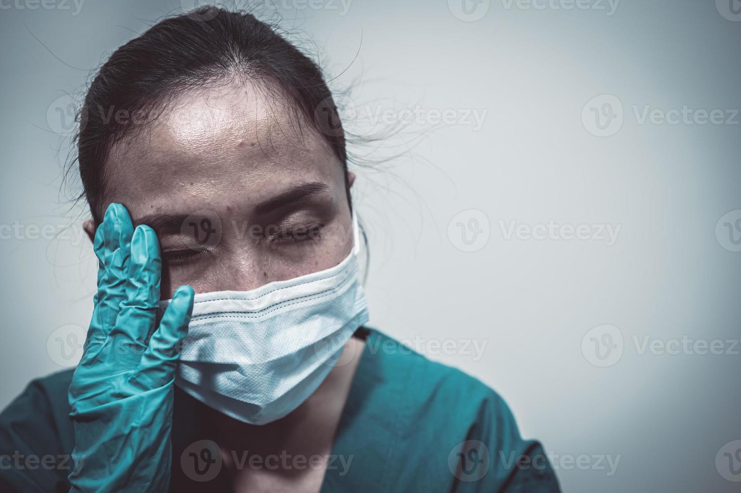 Tired depressed female asian scrub nurse wears face mask blue uniform sits on hospital floor,Young woman doctor stressed from hard work photo