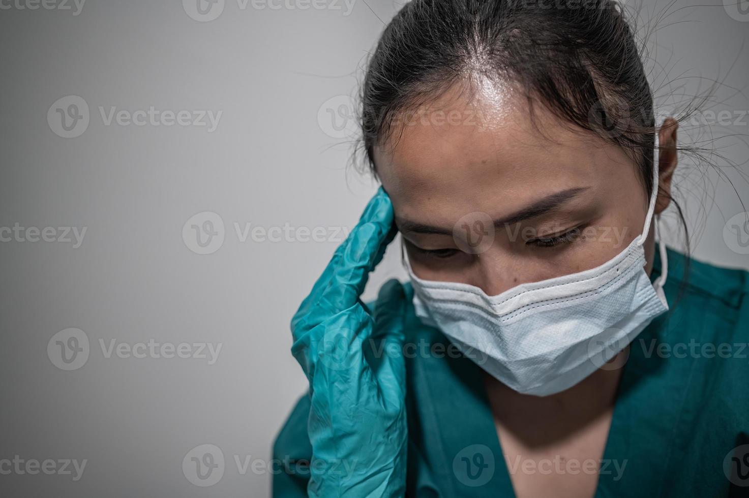 una enfermera asiática cansada y deprimida usa una máscara facial uniforme azul sentada en el piso del hospital, una joven doctora estresada por el trabajo duro foto