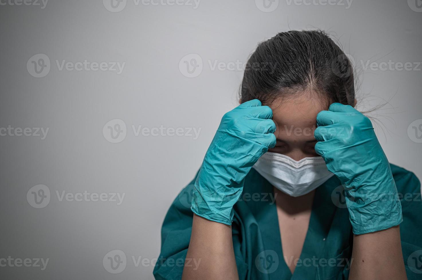 una enfermera asiática cansada y deprimida usa una máscara facial uniforme azul sentada en el piso del hospital, una joven doctora estresada por el trabajo duro foto