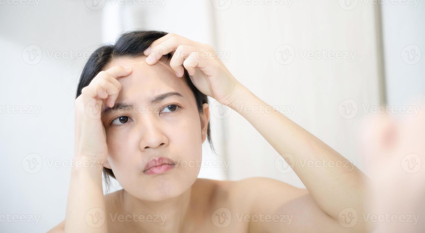Problem skin. Concerned young asian women popping pimple on cheek while standing near mirror in bathroom. young asian women with acne photo