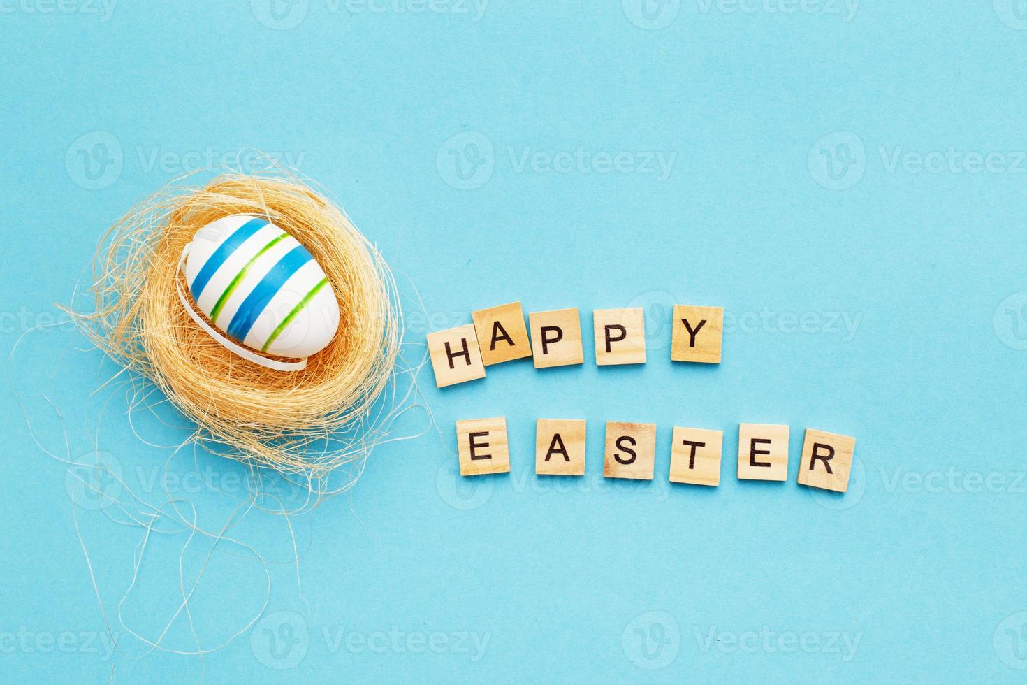 inscription happy easter with colorful handmade painted egg in the nest on blue background photo
