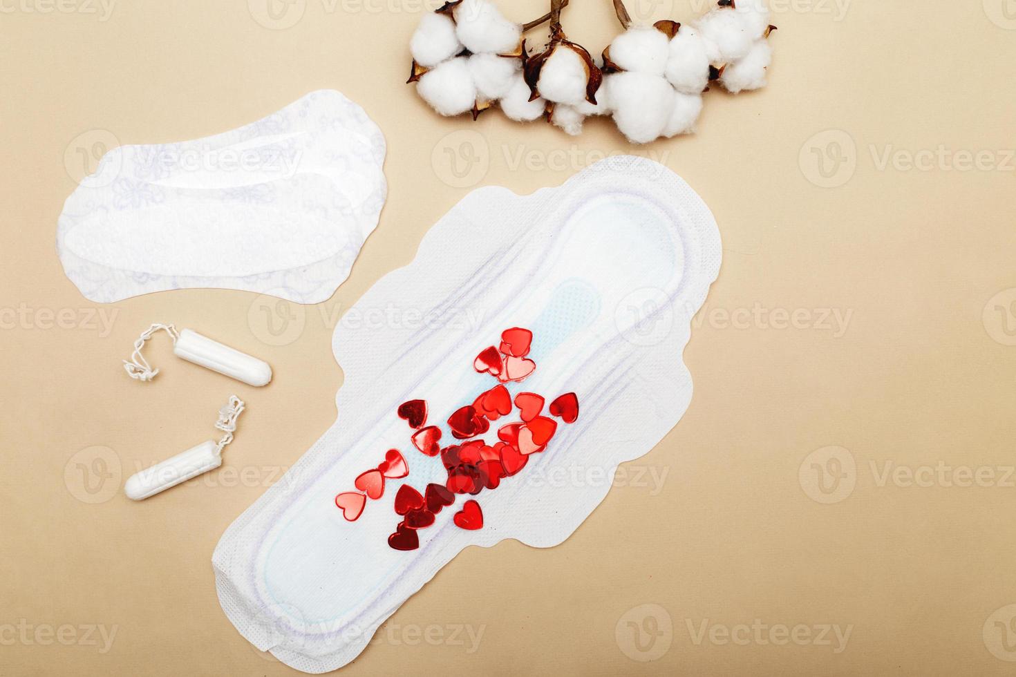 Women's hygiene pads with tampons, flower cotton on a beige background with red hearts photo