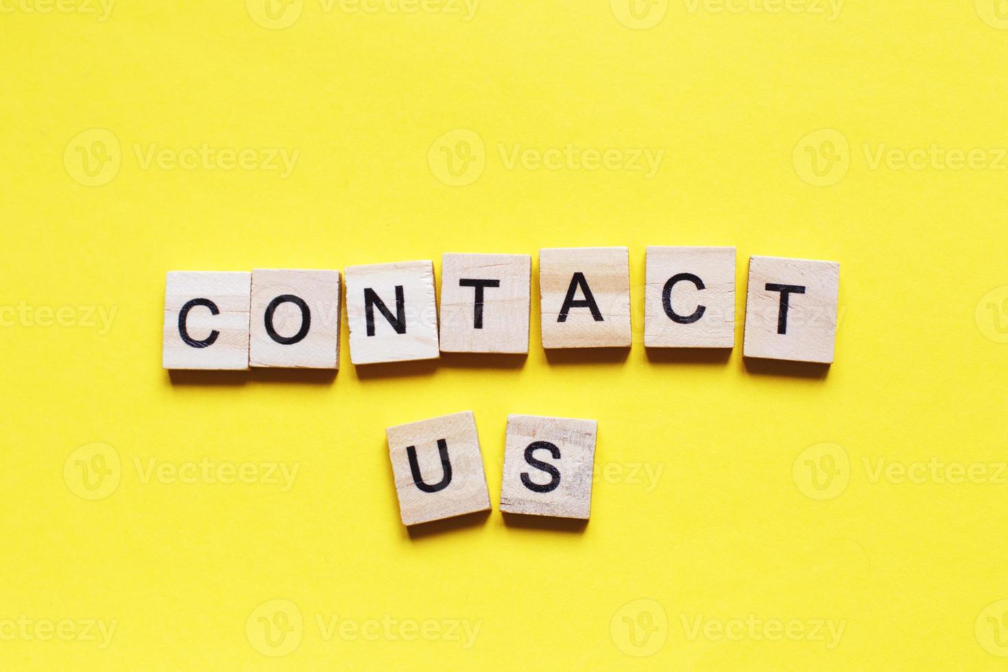 Word contact us made from wooden cubes on a yellow paper background. photo
