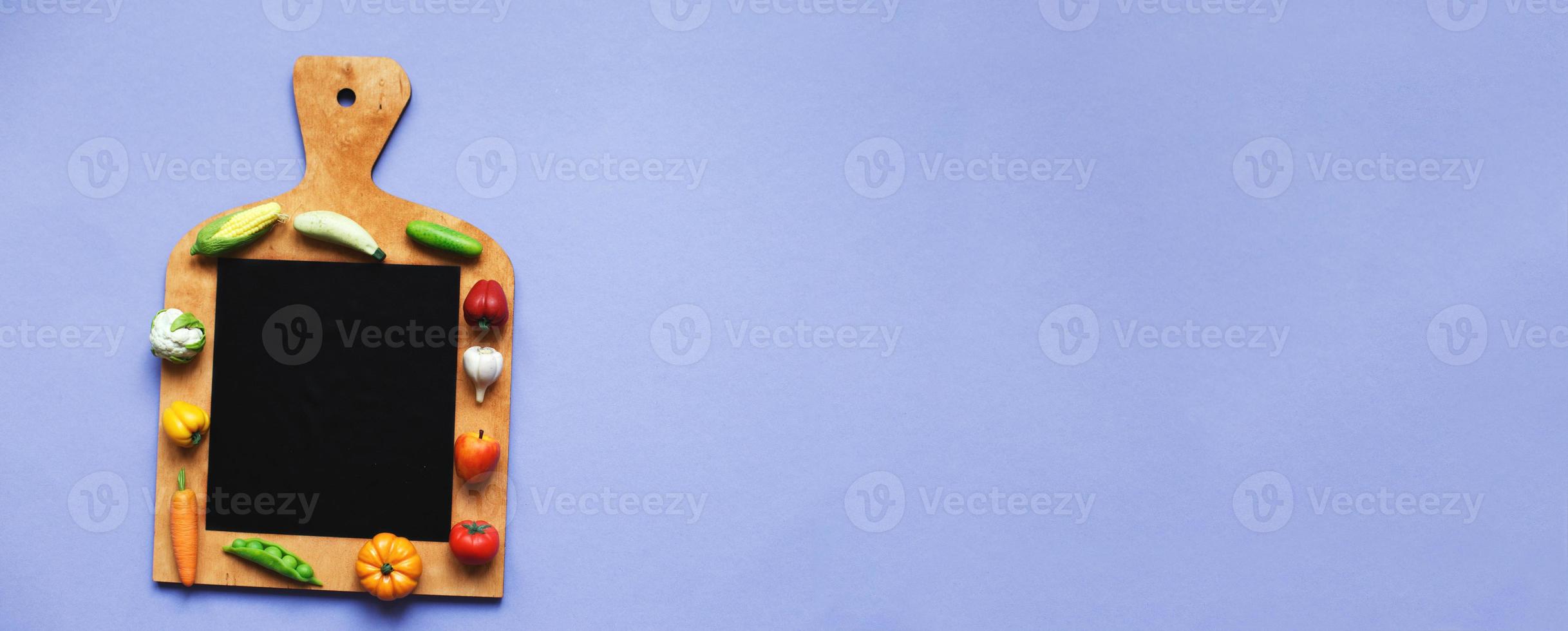 vegetables and fruits on the cutting board on purple background. healthy cooking concept photo