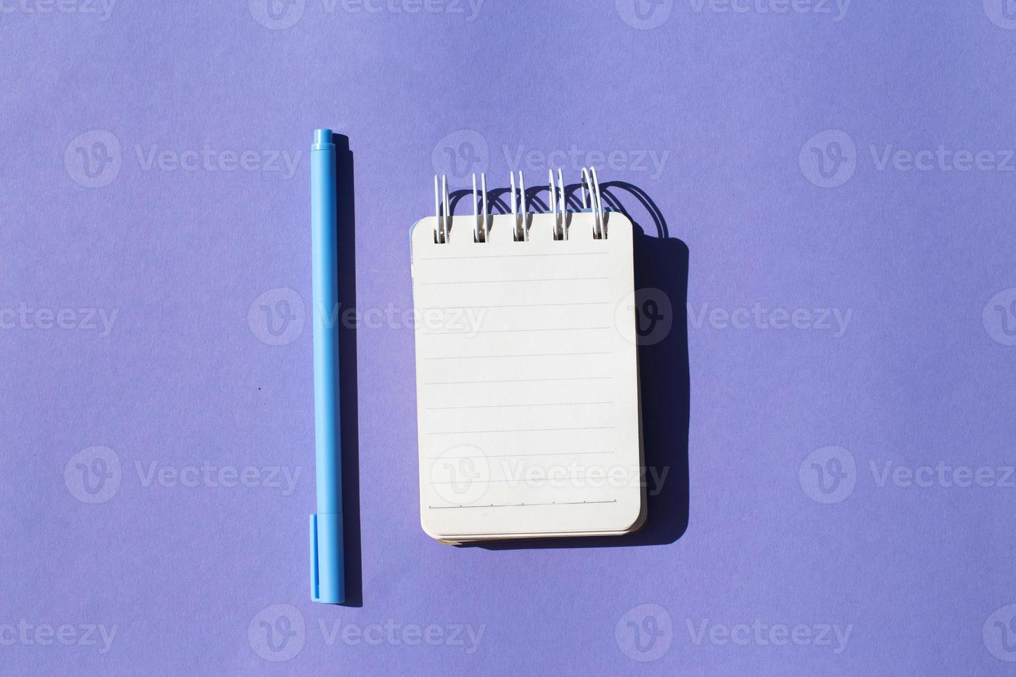Top view of blank note paper with pen on purple background photo