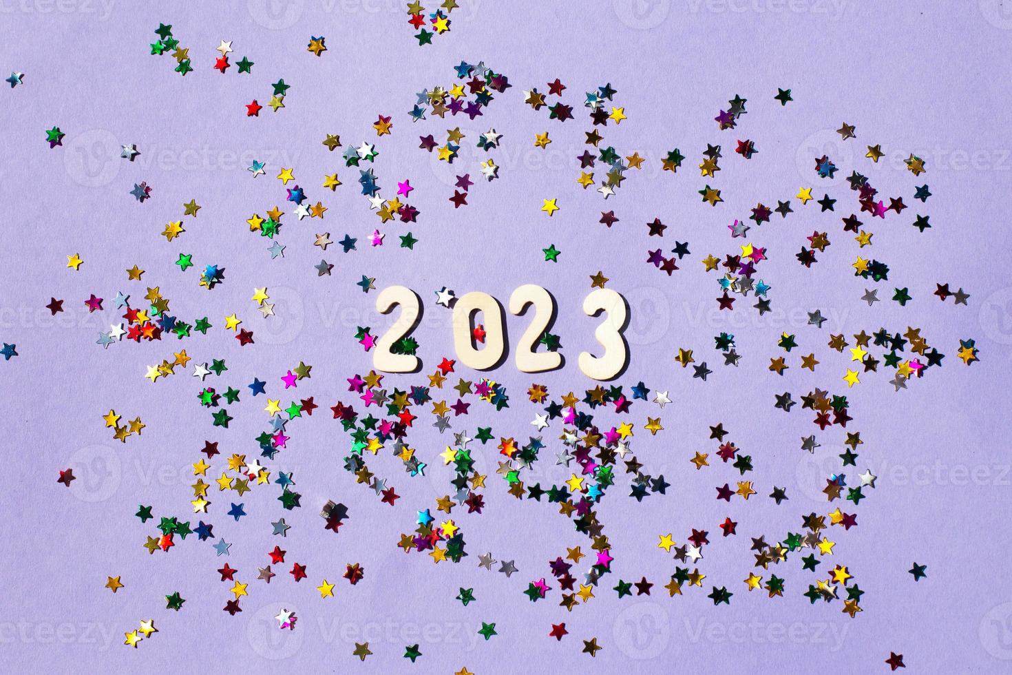 inscription 2023 with wooden numbers on purple background with multicolored confetti.Festive concept photo