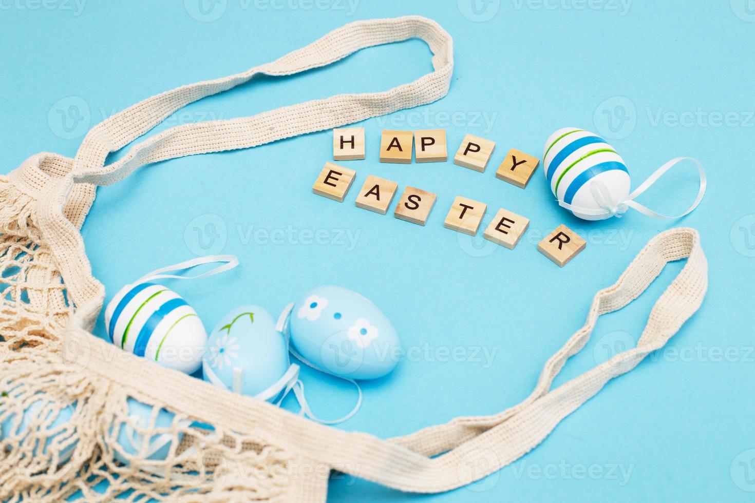 inscription happy easter with colorful painted eggs and cotton string bag on blue background photo