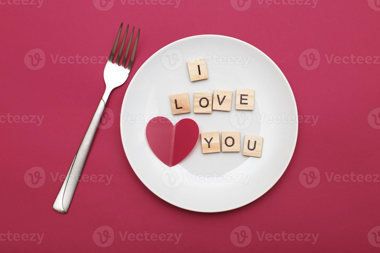 inscription i love you with a heart on a white plate with fork on red background photo