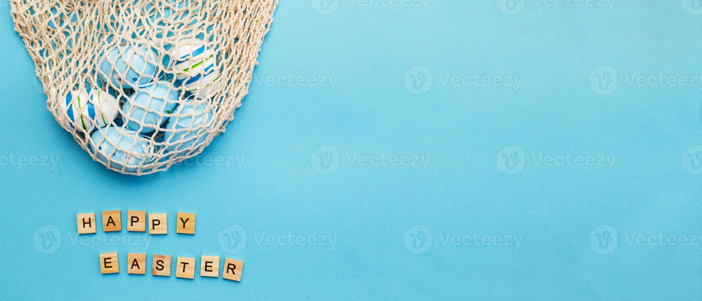 inscription happy easter with colorful painted eggs and cotton string bag on blue background photo
