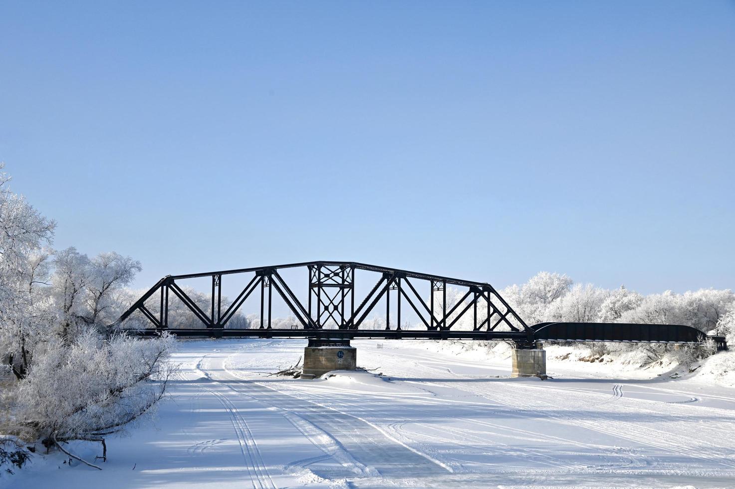 a railway bridge over a frozen river with frost covered trees on the shore photo