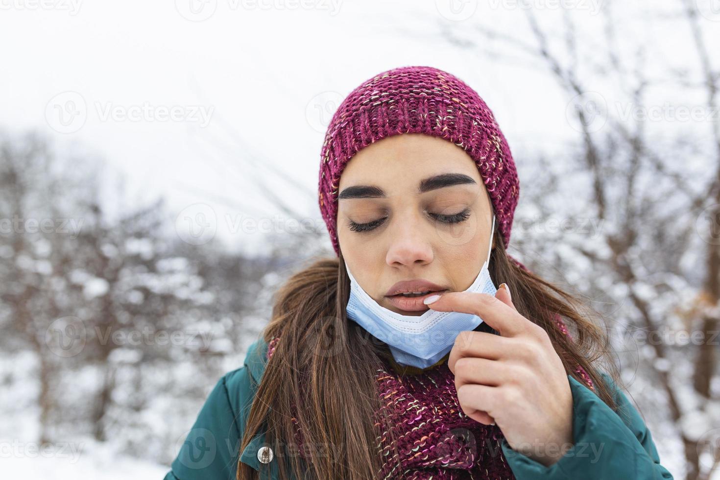 Don't touch your face, stop spreading Coronavirus. Young woman touching her mouth with dirty hand. Avoid touching your face. Woman putting down face mask rubbing her lip outdoor. photo