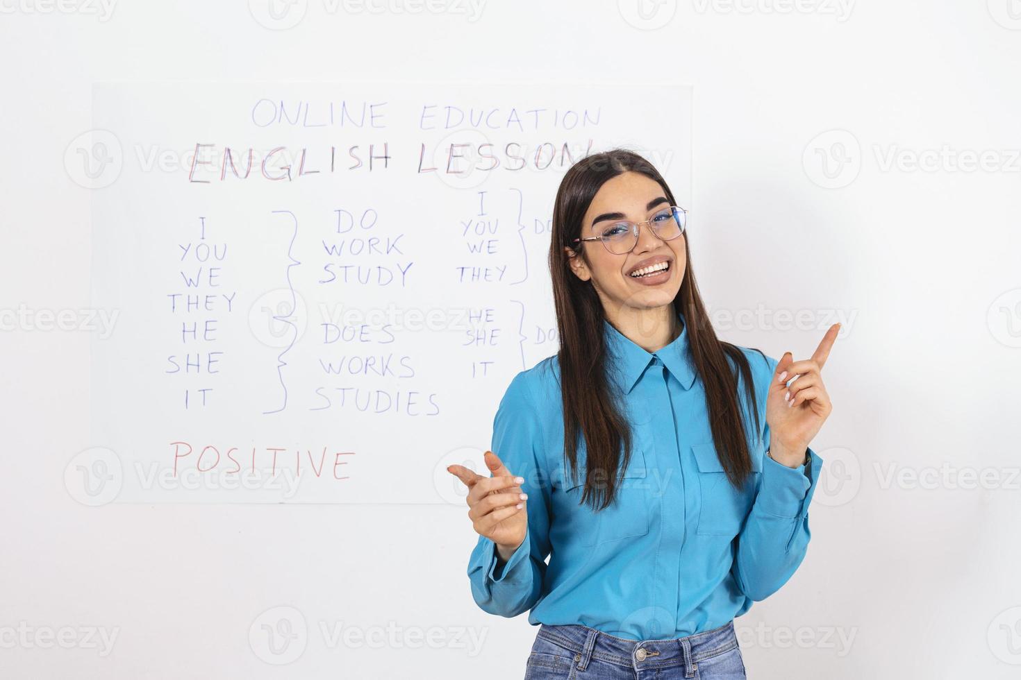 educación moderna de forma remota. una joven alegre señala la pizarra y explica las reglas del inglés en línea foto