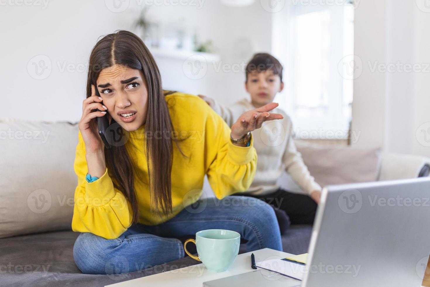 A working mother multitasking. Single mother with a kid trying to work. Worried woman working at home while her son is not letting her. Quarantine isolation during the Covid-19 health crisis photo