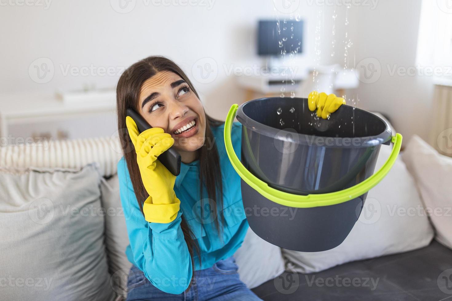 mujer sorprendida llamando a un plomero mientras recolectaba agua que se escapaba del techo usando un utensilio foto