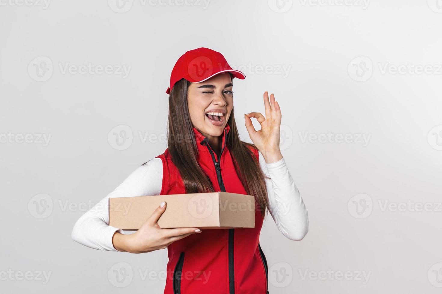 imagen de una joven y emocionada repartidora con gorra roja parada con un buzón de paquetes aislado sobre fondo blanco. mirando la cámara. foto