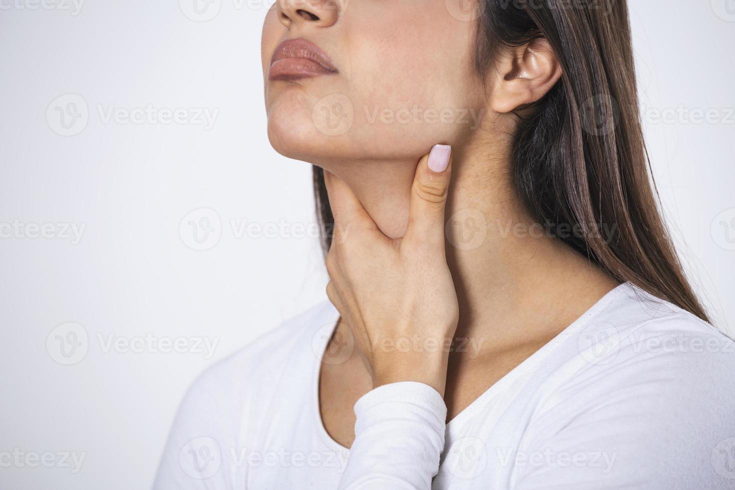 Young beautiful woman suffering from pain in throat, touching inflamed zone on her neck, cropped, empty space, sore throat photo