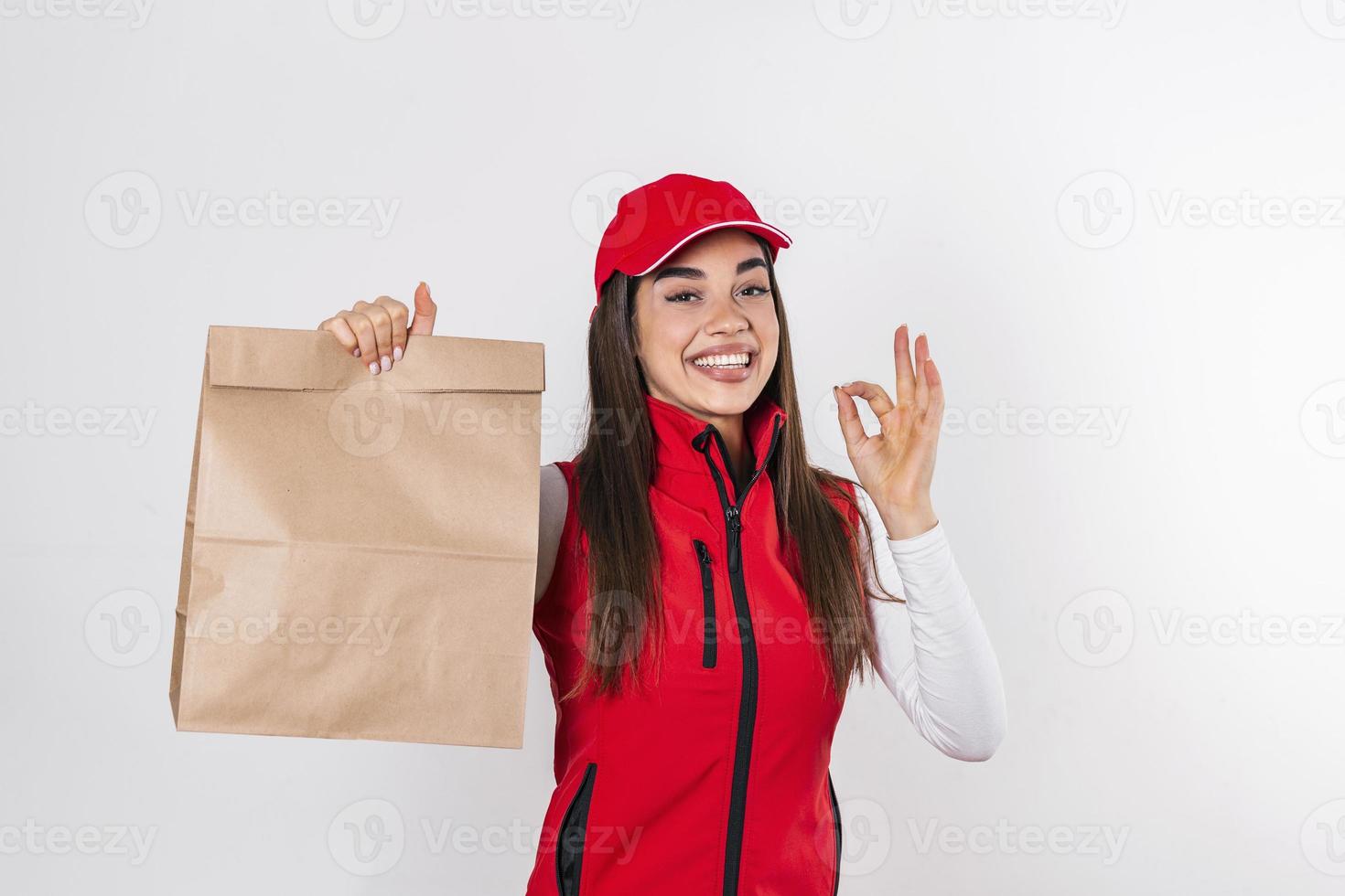 Delivery woman in red uniform hold craft paper packet with food isolated on white background, studio portrait. Female employee in cap t-shirt print working as courier. Service concept. photo