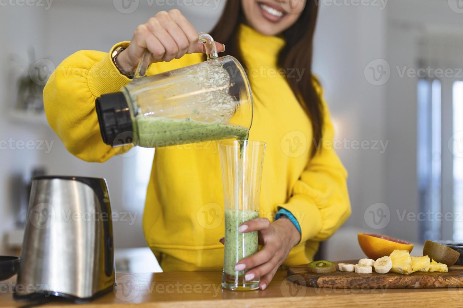 mujer joven vertiendo batido en vaso. hermosa mujer sonriente mostrando bebida energética llena de vitaminas. dieta de alimentos crudos, nutrición vegetariana, comida de desintoxicación orgánica foto