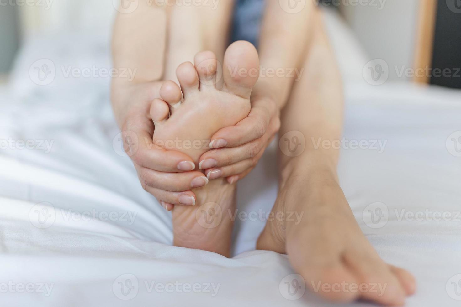 dolor de pies mujer sentada en la cama sosteniendo sus pies en casa con pies dolorosos y fatiga de los músculos estirados para aliviar el dolor. concepto de salud foto