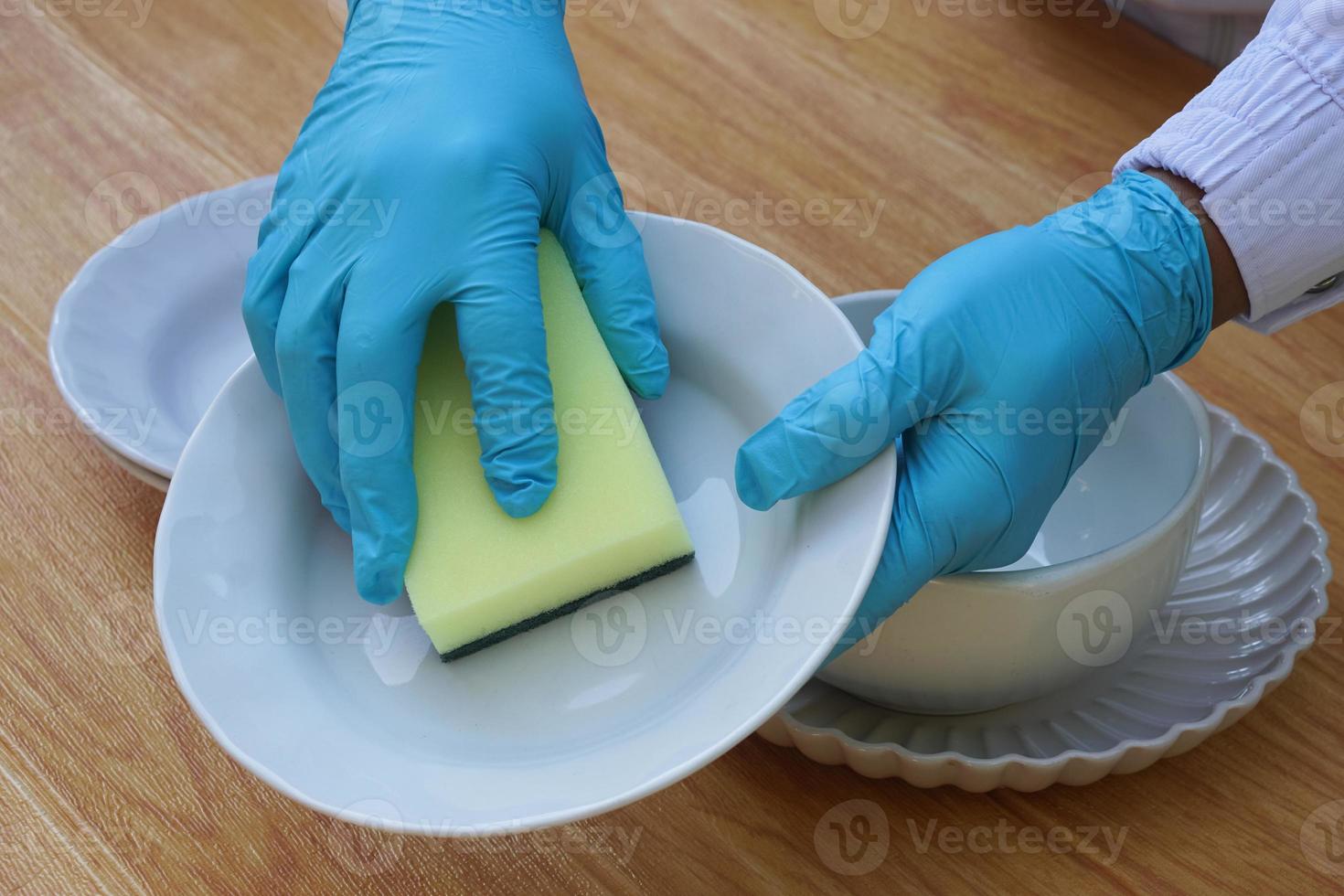 Hands use sponge scrubber to clean dish. Concept, daily chore, household cleaning kitchen utensils. Wear protective gloves to protect hands from chemical substances allergy. photo