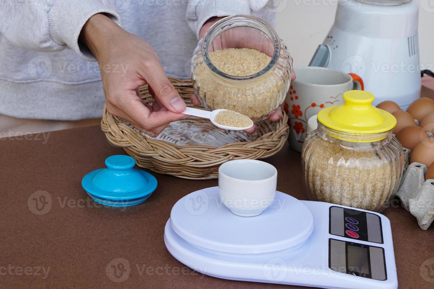 Closeup hand holds spoon of sugar to scale. Measuring sugar Concept, cooking. bakery. Love cooking lifestyle. Pastime activity. Kitchen.  Weighing food ingredient. photo