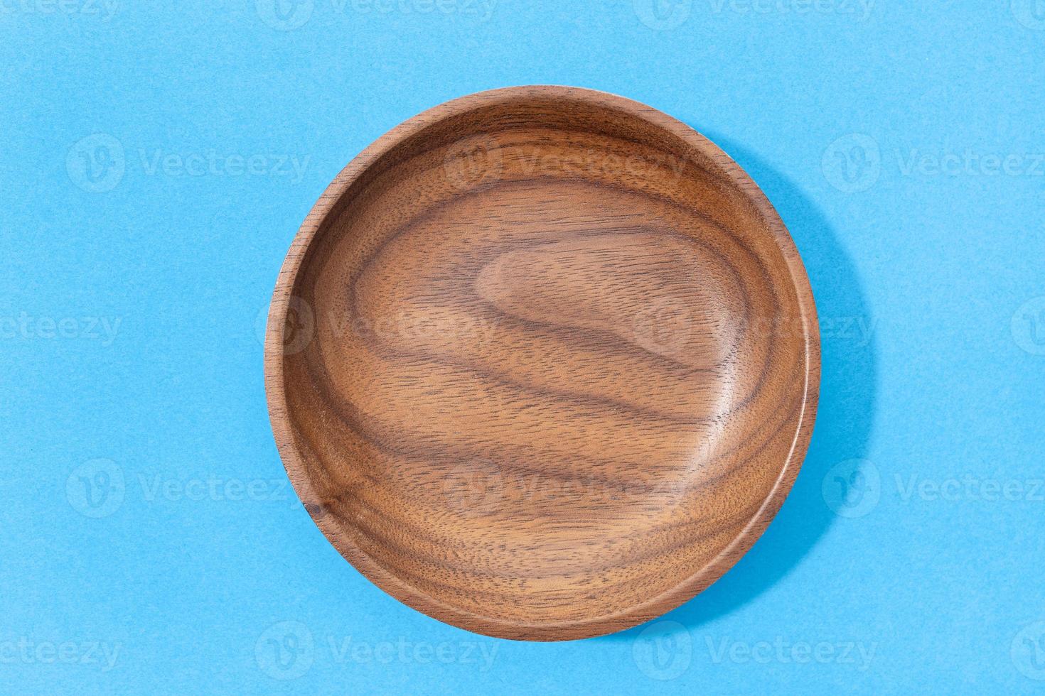 Empty round wooden plate or bowl isolated on blue background. Walnut wood. Top view photo