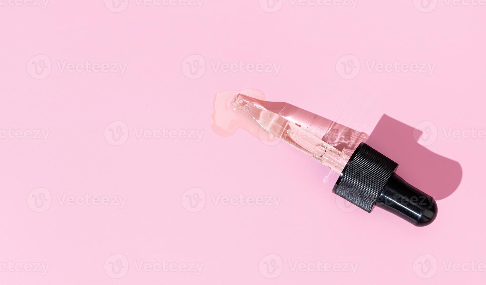 Flat lay of a pipette with pouring liquid serum on pink background. Copy space photo