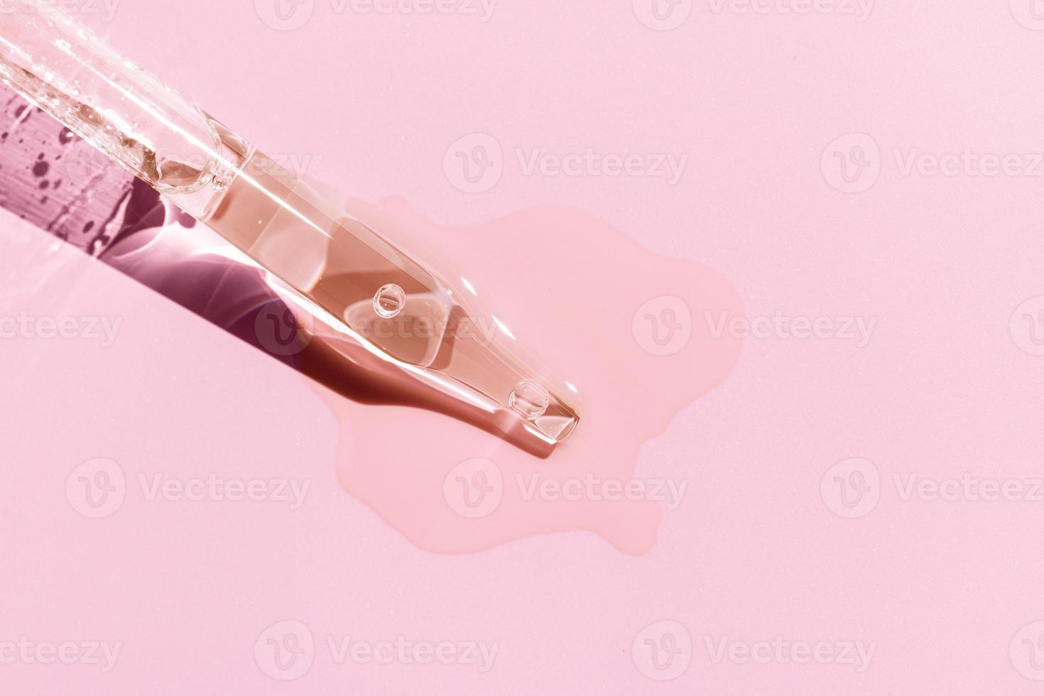 Close up of a pipette with pouring liquid serum on pink background. Copy space photo
