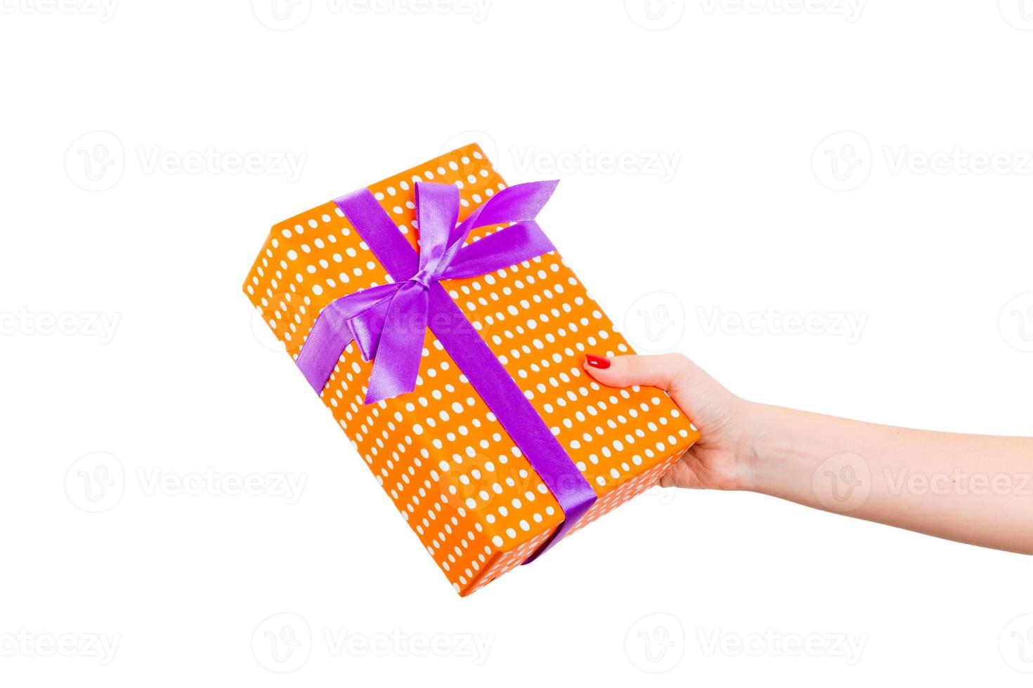 las manos de las mujeres dan Navidad envuelta u otro regalo hecho a mano en papel naranja con cinta morada. aislado sobre fondo blanco, vista superior. concepto de caja de regalo de acción de gracias foto