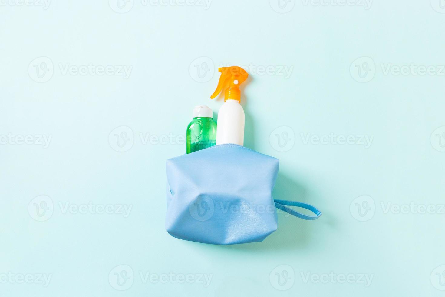 Top view of female cosmetics bag full of suncream spray, sunsreen, sunblock and body lotion and spf cream on blue background with copy space. Directly above. Bright summer concept photo