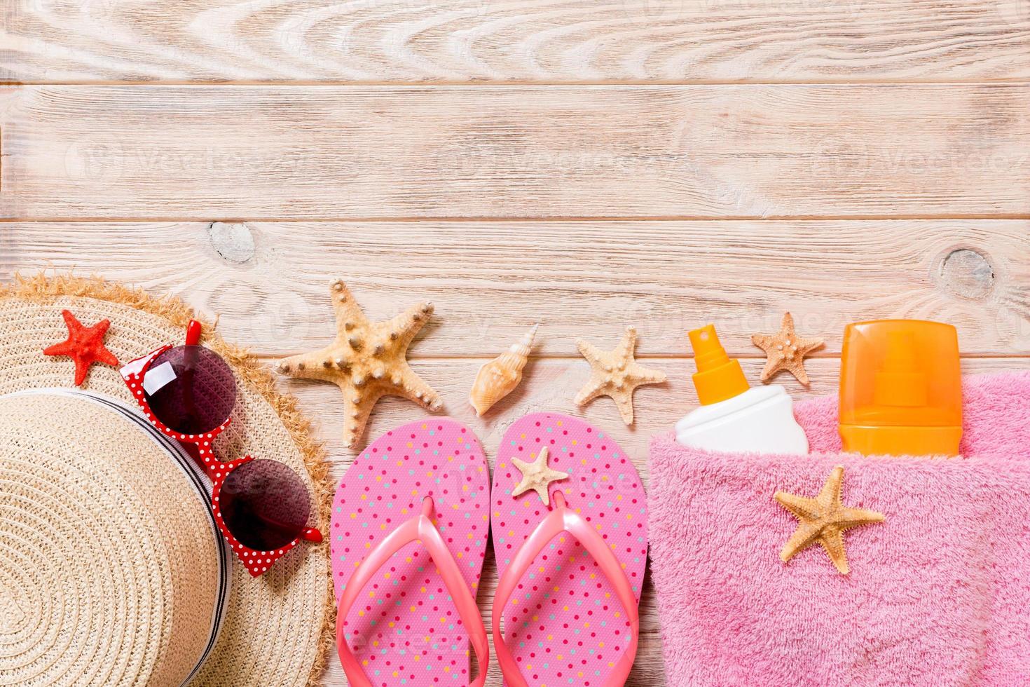 flip flops, straw hat, starfish, sunscreen bottle, body lotion spray on wooden background top view . flat lay summer beach sea accessories background, travel concept photo