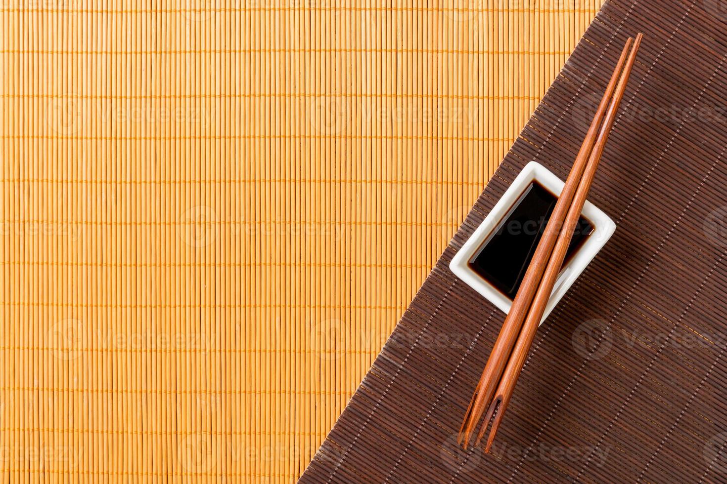 Chopsticks and bowl with soy sauce on two bamboo mat blak and yellow top view with copy space photo
