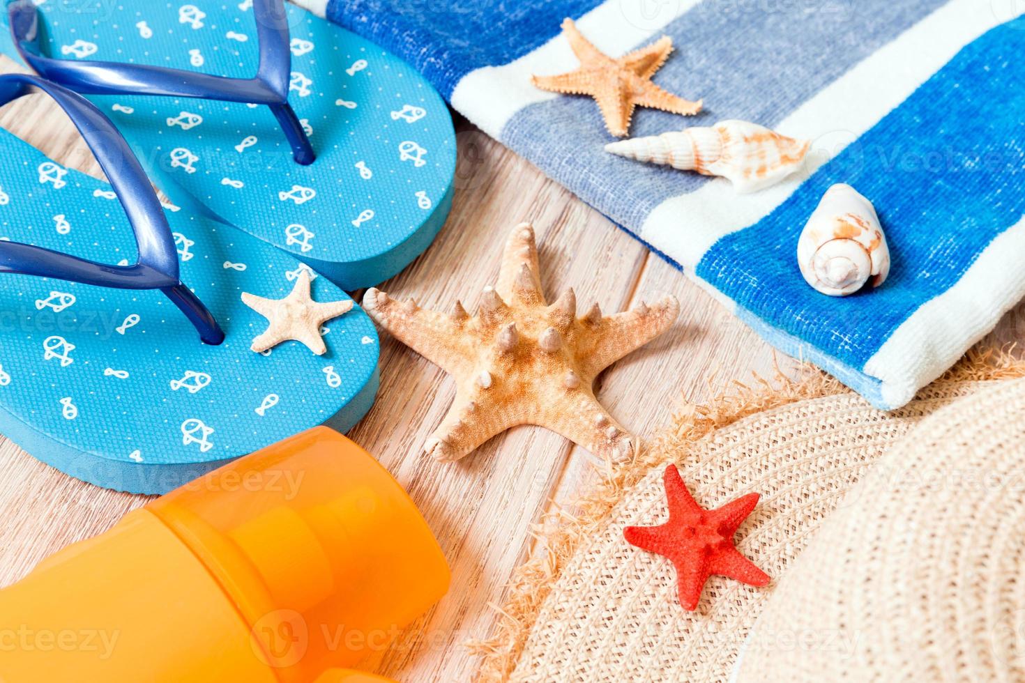 chanclas, sombrero de paja, estrellas de mar, botella de protector solar, spray de loción corporal en la vista superior de fondo de madera. fondo plano de accesorios de mar de playa de verano, concepto de vacaciones foto