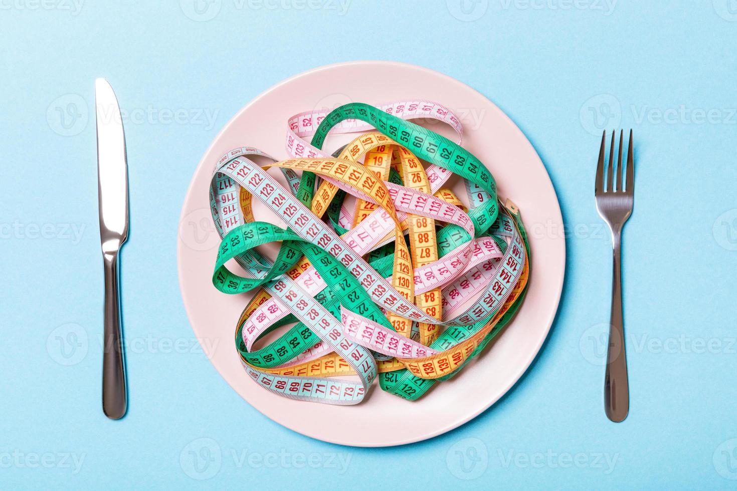 Heap of colorful measuring tape instead of spaghetti in round plate on blue background. Top view of healthy eating concept photo