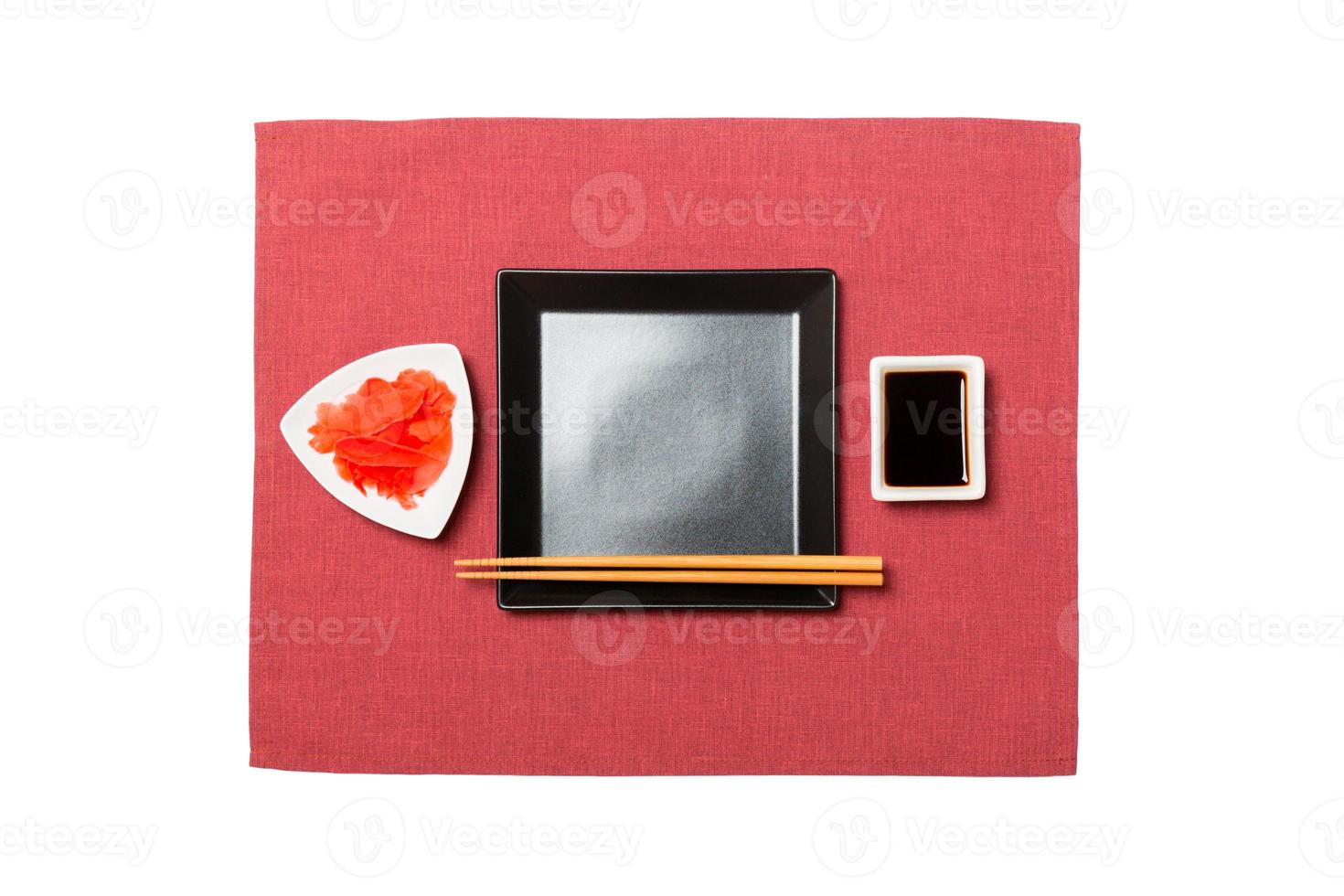 Empty black square plate with chopsticks for sushi, ginger and soy sauce on red napkin background. Top view with copy space for you design photo