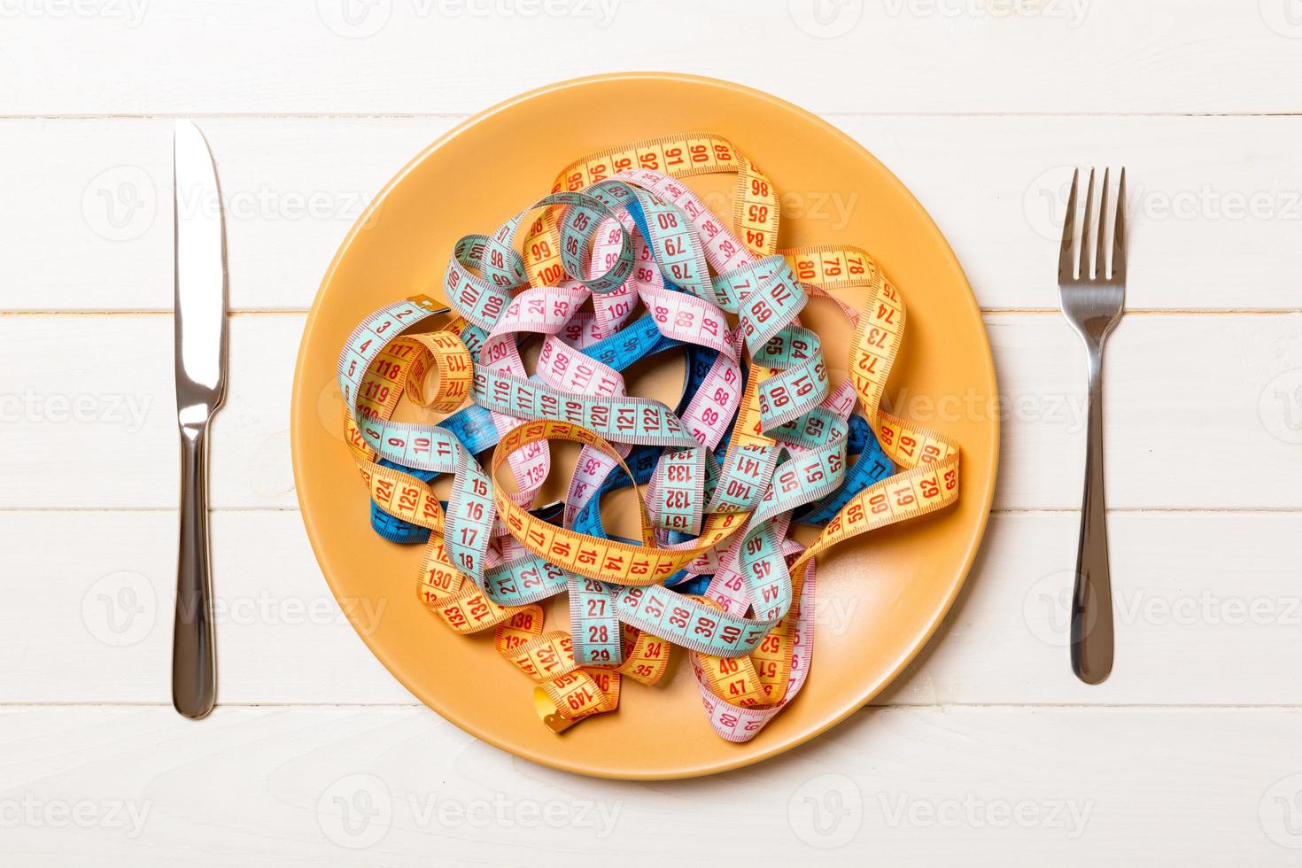 Heap of colorful measuring tape instead of spaghetti in round plate on wooden background. Top view of healthy eating concept photo