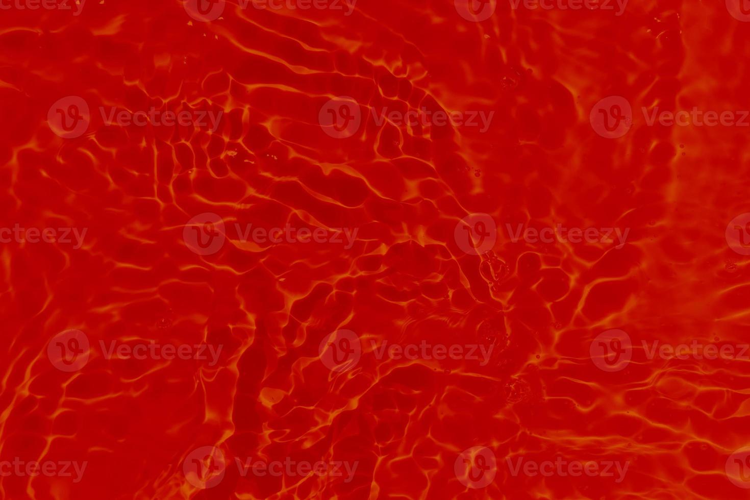 Defocus blurred transparent red colored clear calm water surface texture with splashes and bubbles. Trendy abstract nature background. Water waves in sunlight with caustics. Red water shinning photo