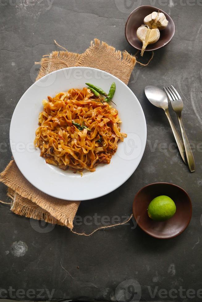 kwetiau goreng es un plato de fideos de arroz plano salteado indonesio chino hecho de kwetiau, salteado en aceite de cocina con ajo, cebolla, ternera, pollo, gambas fritas, cangrejo y otras verduras foto