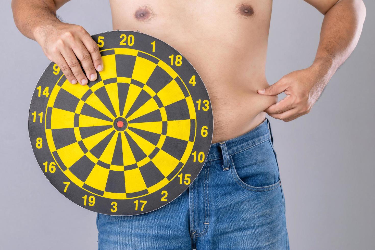 Fat people holding round yellow dartboard beside his belly position. Target of losing weight concept. Studio shot isolated on grey photo