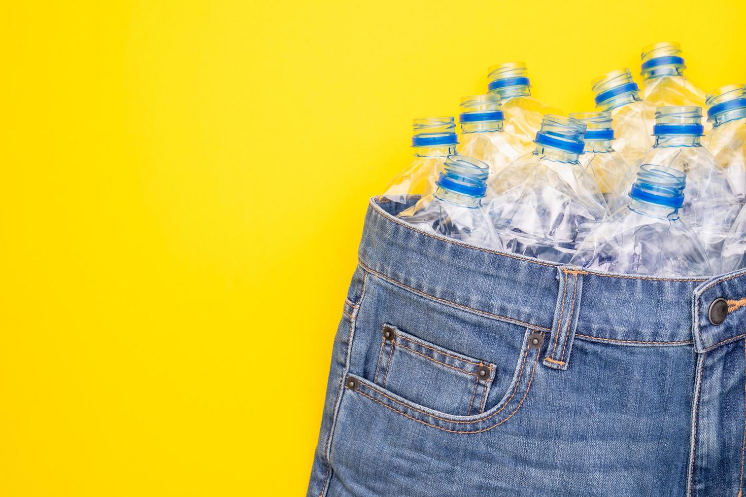 Recycle technology of plastic bottle to make clothes. Top view old water bottle and blue short jeans on yellow photo