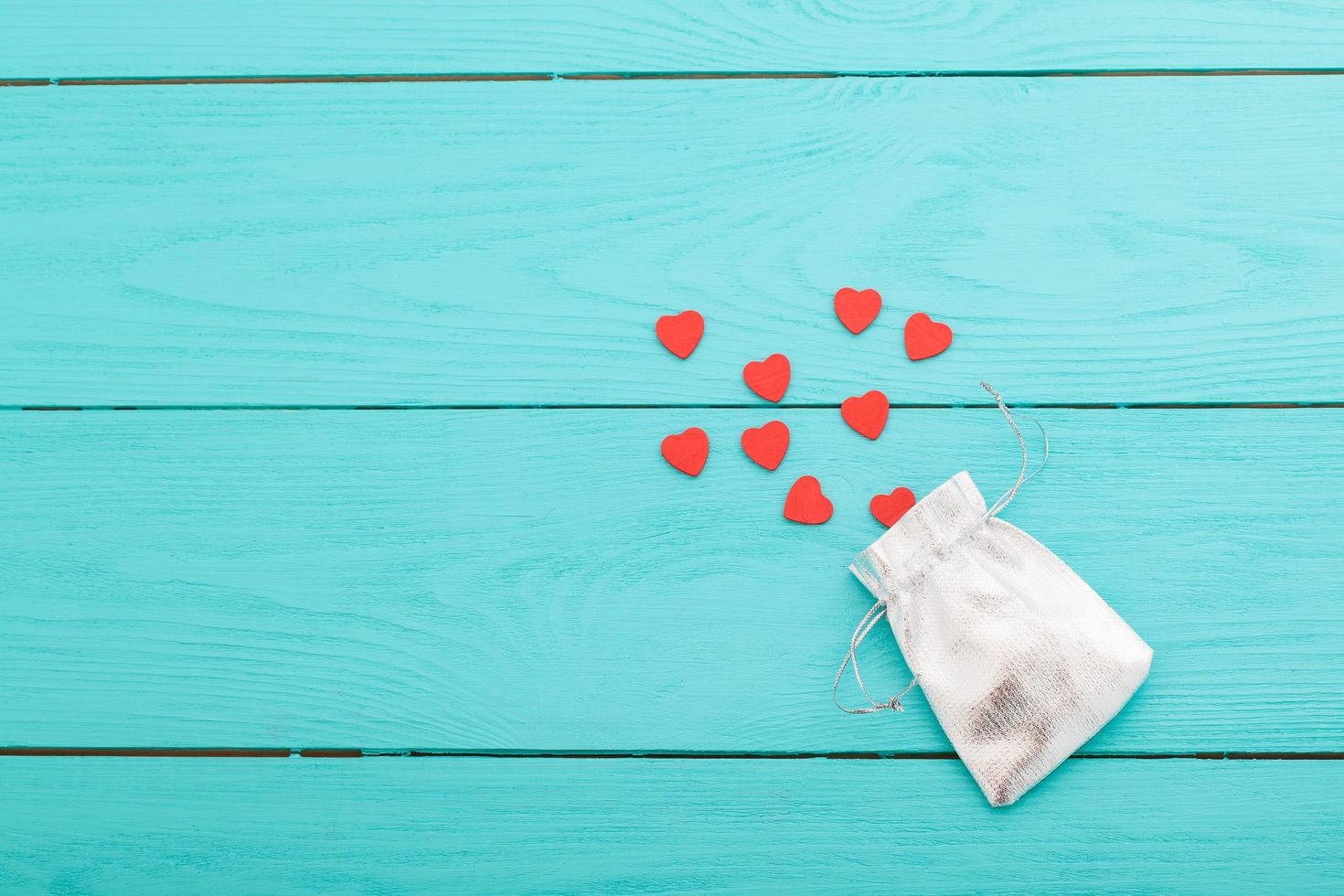 primer plano de una pequeña bolsa de plata brillante llena de lindos corazones de terciopelo rojo sobre fondo rojo. concepto de un regalo de amor romántico para parejas, día de san valentín, matrimonios o cumpleaños. foto