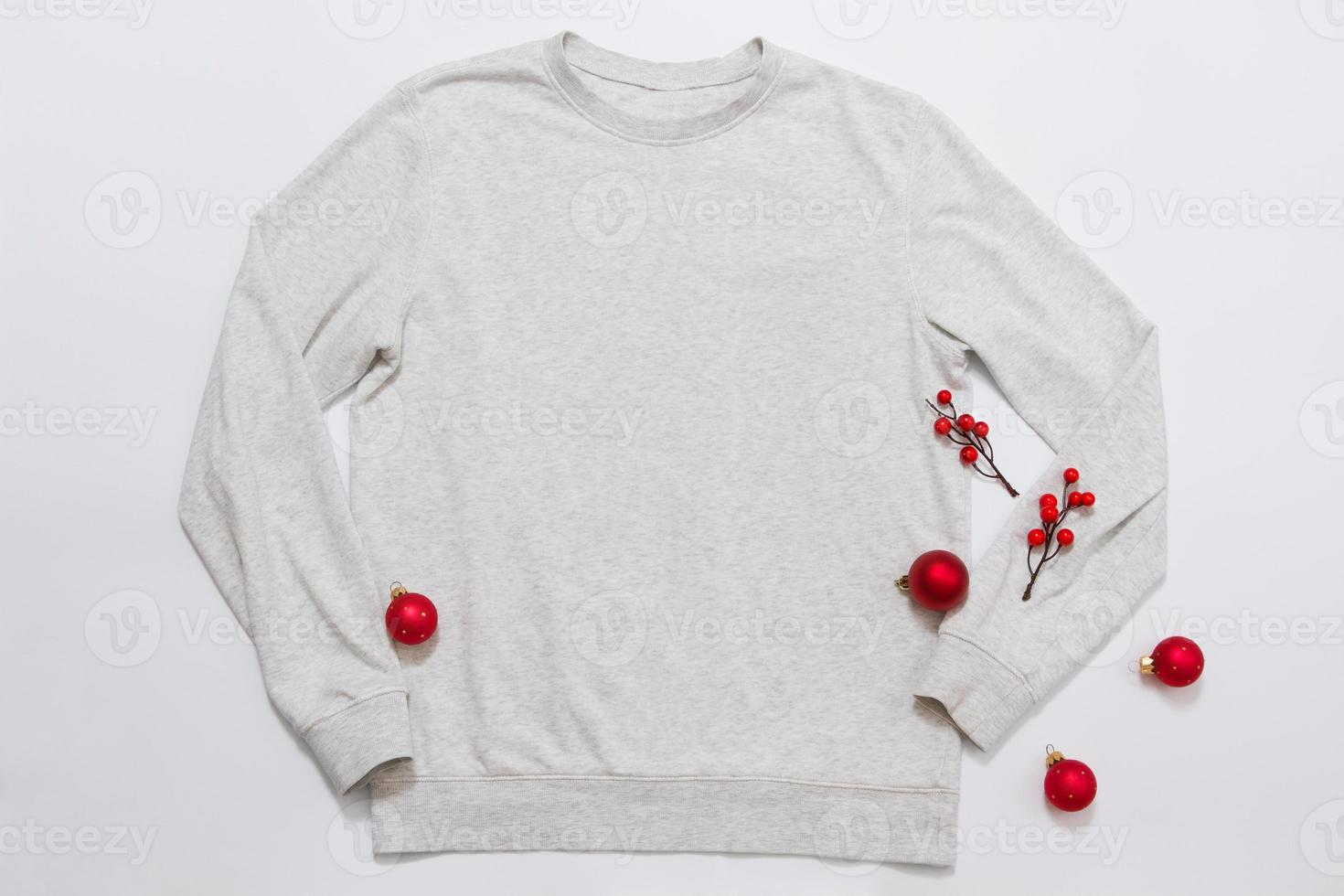 Close up white blank template sweatshirt with copy space and Christmas Holiday concept. Top view mockup hoodie and red holidays decorations on white background. Happy New Year accessories. Xmas outfit photo