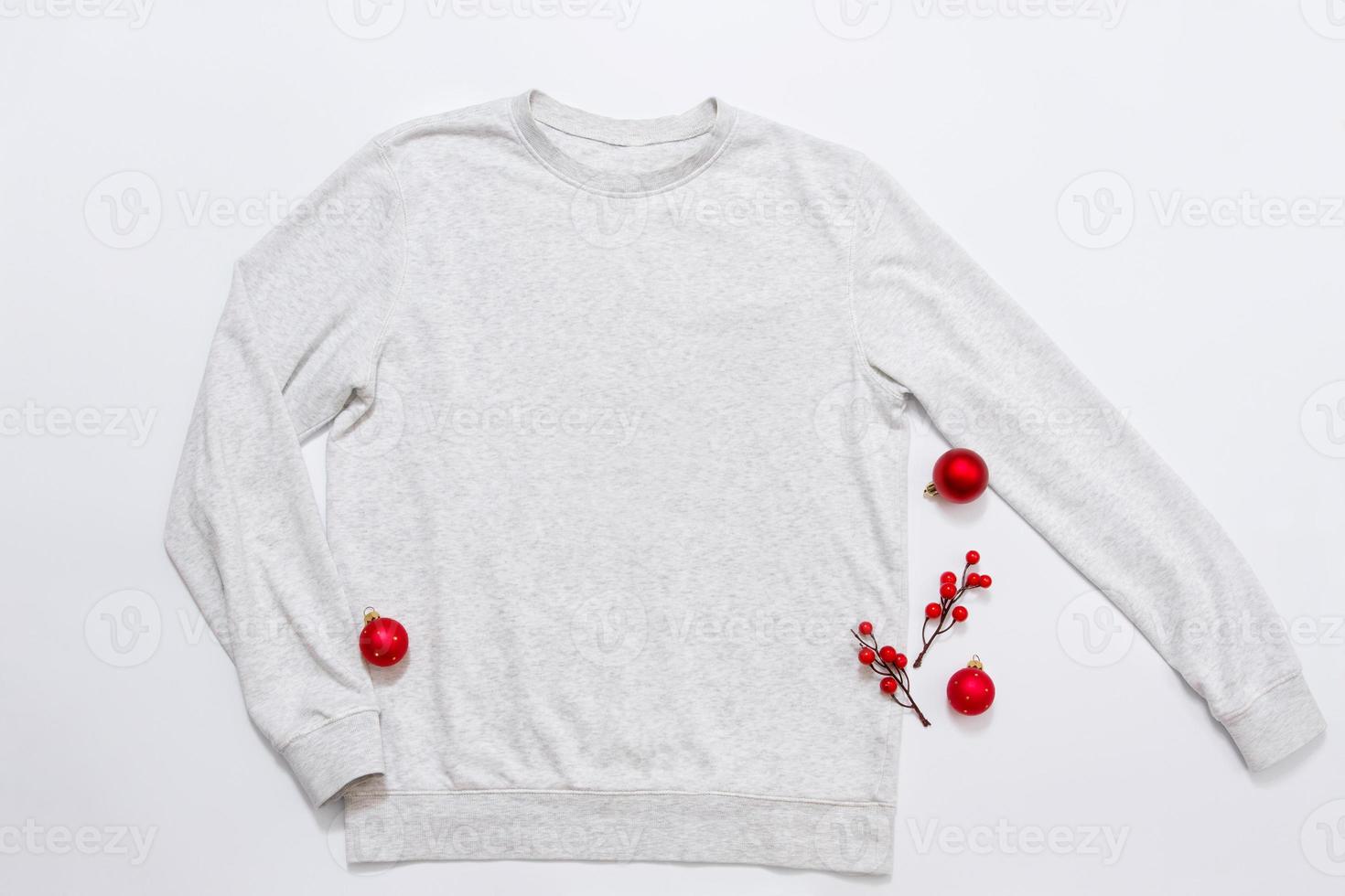 Close up white blank template sweatshirt with copy space and Christmas Holiday concept. Top view mockup hoodie and red holidays decorations on white background. Happy New Year accessories. Xmas outfit photo