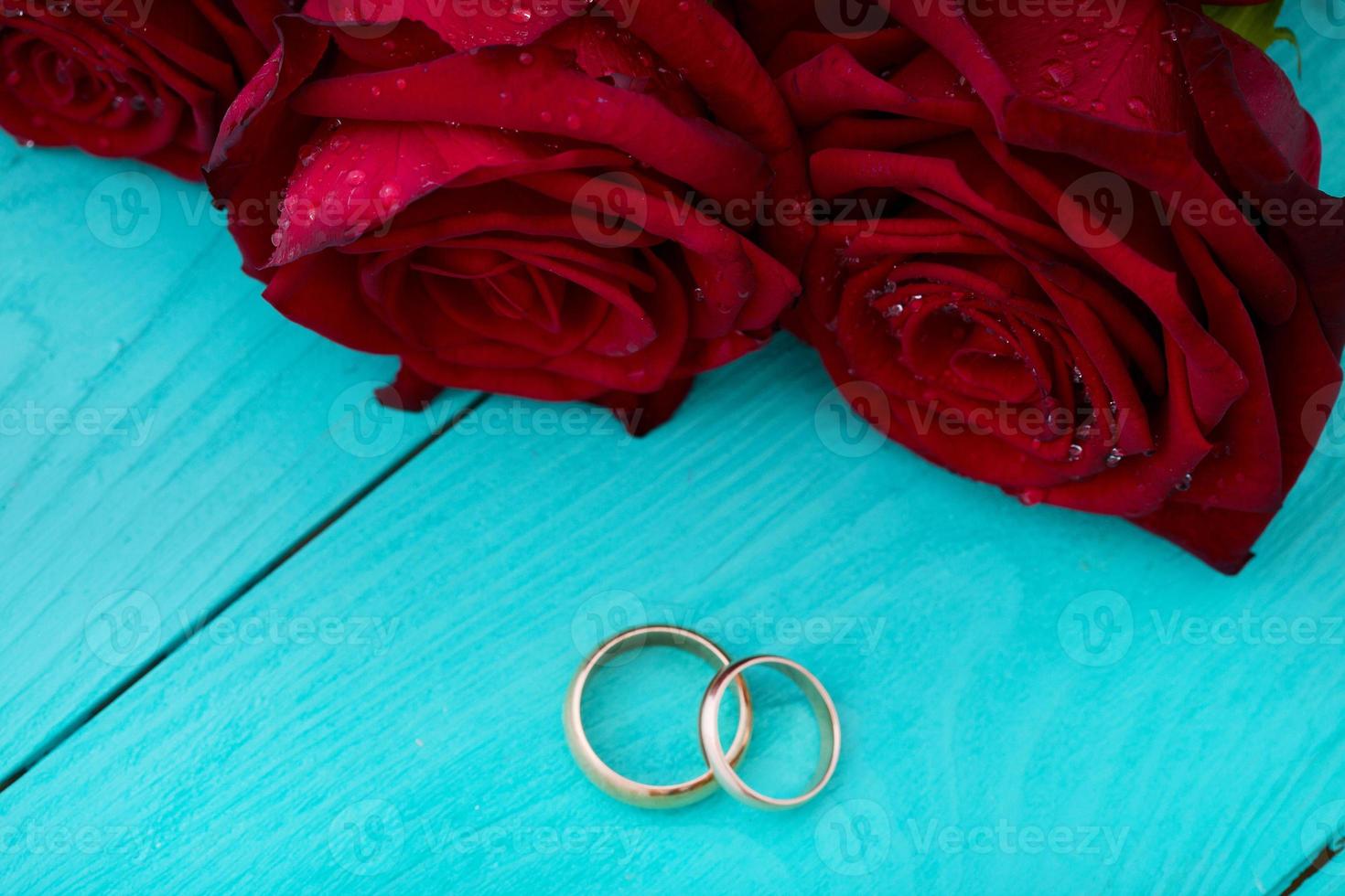Wedding rings and red roses. Wedding bouquet on blue wooden background. Selective focus. Copy space photo