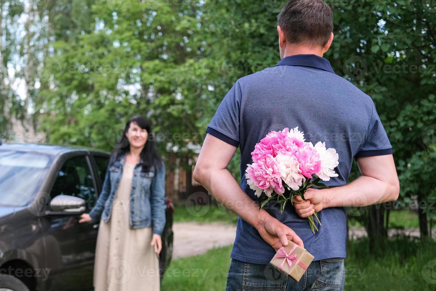 A man holds a bouquet of flowers and a gift behind his back for his girlfriend photo