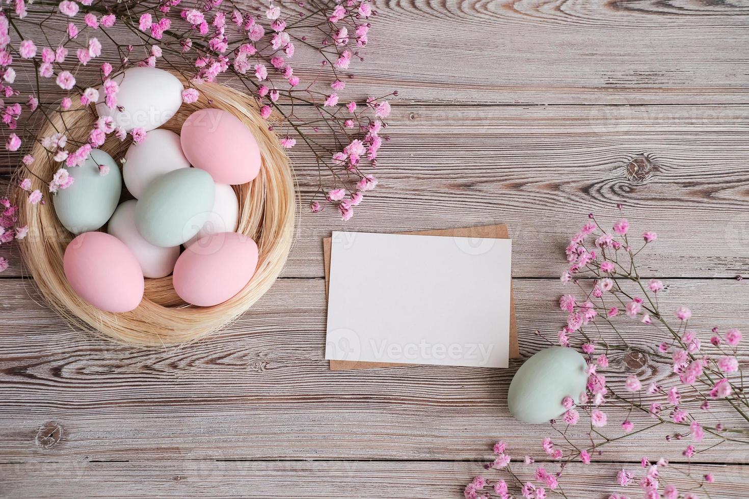 Pink flowers, a nest with eggs in soft pastel colors and blank white card for text on a wooden background. Mockup. Place for text. Easter card photo