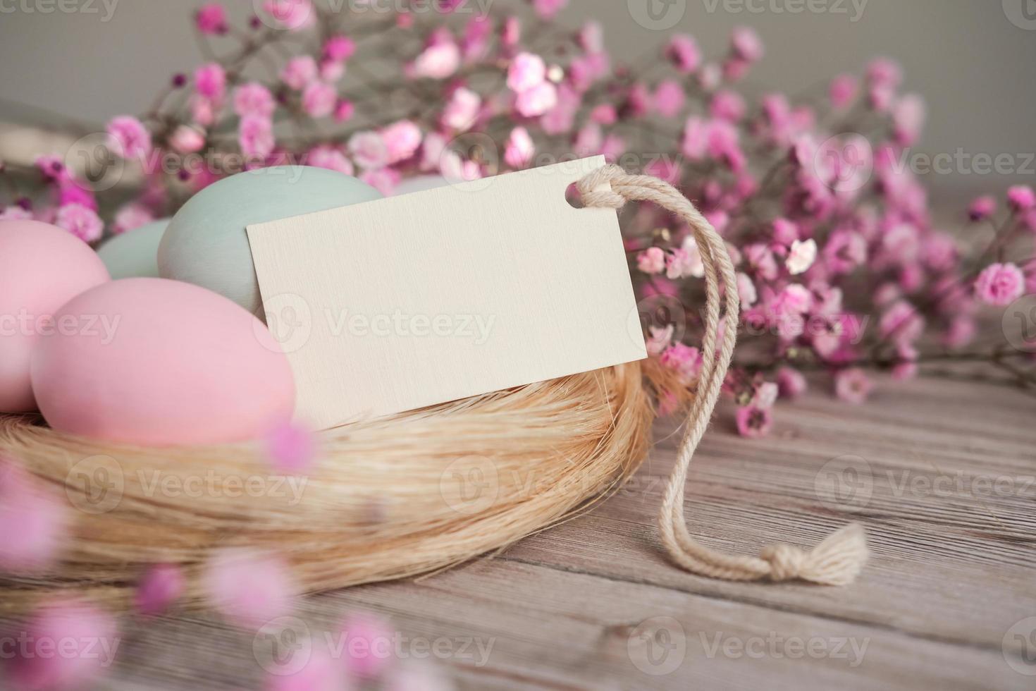 Nest with eggs in soft pastel colors and blank white card for text. Mockup tag. Easter card photo